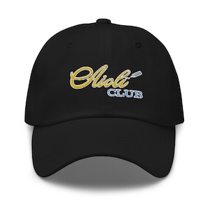 Pode incluir: Boné de beisebol preto com um logotipo bordado em ouro que diz "Aioli Club" com uma pequena imagem de uma garrafa de espremer.