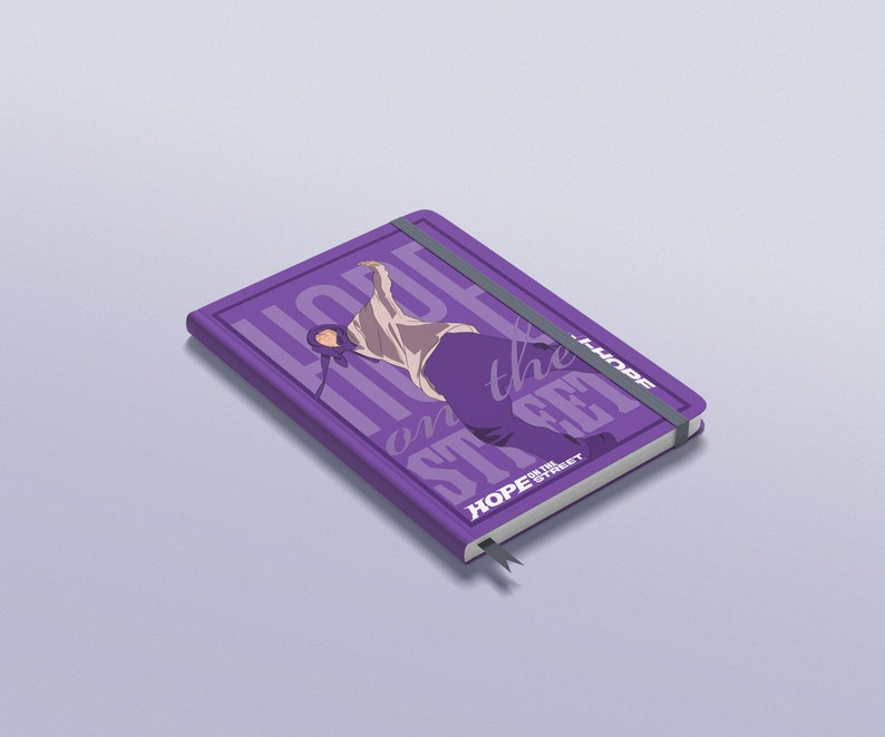 Puede incluir: Cuaderno morado con un gr&aacute;fico de una persona bailando y el texto "HOPE on the STREET" en blanco. El cuaderno tiene una banda el&aacute;stica morada y un marcador de cinta morado.