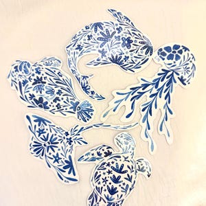 May include: A collection of blue and white stickers featuring marine life designs. The stickers include a whale, jellyfish, stingray, sea turtle, and other sea creatures, all decorated with floral patterns.