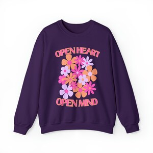 May include: A dark purple sweatshirt with a floral design. The design features various flowers in shades of pink, orange, and white. The words "OPEN HEART" and "OPEN MIND" are printed above and below the flowers in a matching orange color.