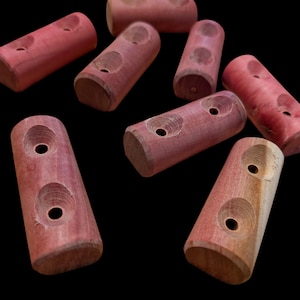 May include: Eight reddish-brown wooden dowels are displayed against a black background. Each dowel is cylindrical with rounded ends and two circular holes carved into the surface. The dowels are scattered.
