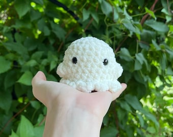 May include: A white crocheted octopus plush toy with black eyes. The octopus is being held in someone's hand.
