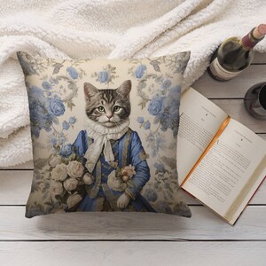 May include: A decorative cushion featuring a vintage illustration of a cat wearing a blue and white dress and holding a bouquet of flowers. The background features a floral pattern with blue roses.
