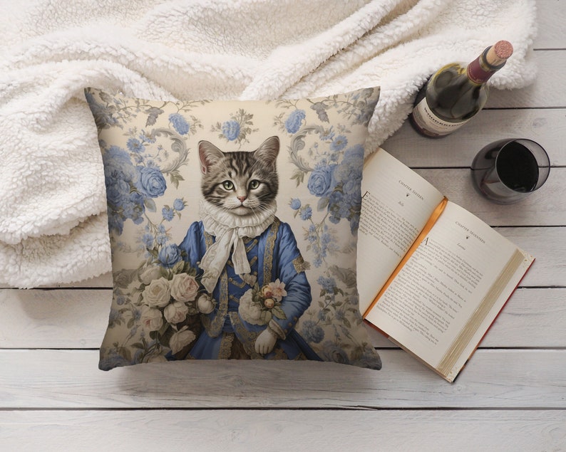 May include: A decorative cushion featuring a vintage illustration of a cat wearing a blue and white dress and holding a bouquet of flowers. The background features a floral pattern with blue roses.