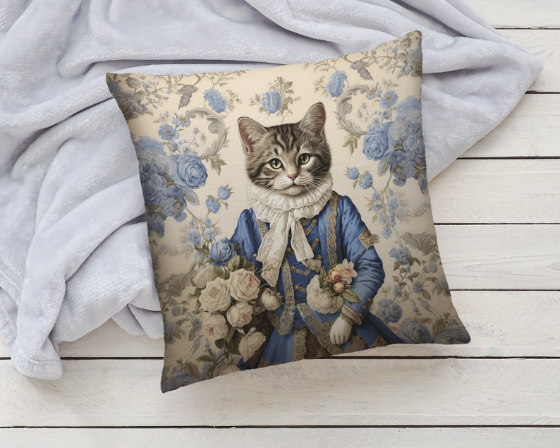 May include: A decorative cushion featuring a cat dressed in a blue and gold suit, holding a bouquet of white roses. The background is a cream-coloured floral pattern with blue flowers.