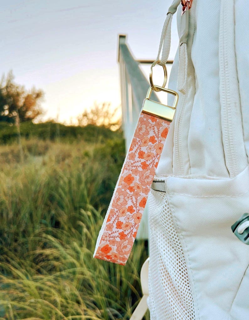 May include: A white backpack with a floral patterned key chain. The key chain is attached to a gold metal ring and has a gold metal clasp. The backpack has a mesh pocket on the side.