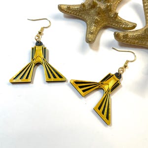 Op de afbeelding: Een paar gouden en zwarte oorbellen in de vorm van de Azadi-toren in Teheran, Iran. De oorbellen zijn gemaakt van hout en hebben gouden haakjes.