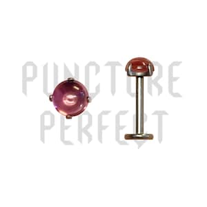 May include: Two pieces of body jewelry. One is a flat-backed stud with a round, pinkish-purple gem. The other is a labret stud with a similar gem. Both have a silver-colored metal setting.