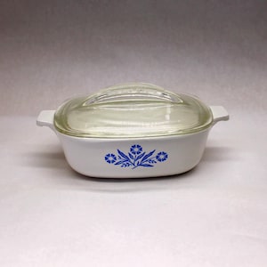 May include: White casserole dish with a clear glass lid. The dish has a blue floral pattern and two handles. The lid has a curved handle. A vintage kitchenware item.