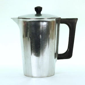 May include: A stainless steel coffee pot with a black handle and lid knob. The pot has a shiny, reflective surface and a spout for pouring. The handle is a dark, solid color, and the lid is a matching metal.