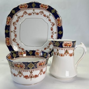 May include: A set of three vintage porcelain teacups with a blue, gold, and red floral pattern. The set includes a creamer, a sugar bowl, and a saucer.