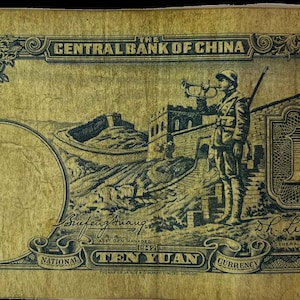 May include: A vintage banknote from the Central Bank of China, featuring a depiction of the Great Wall of China and a soldier blowing a trumpet. The note is dated 1932 and has a value of ten yuan. The note is in good condition and has a yellowed appearance.