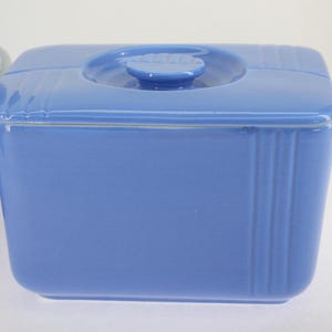 May include: A blue ceramic rectangular dish with a lid. The dish has a white rim and vertical lines on the sides. The lid has a small knob on top.