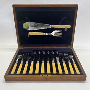 May include: A wooden box with a blue velvet lining contains a set of silver cutlery. The set includes a butter knife, a fork, and 10 dinner forks. The cutlery has ivory handles.