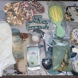 Puede incluir: Una colección de artículos con temática floral, que incluye una toalla blanca con flores amarillas, una diadema con estampado floral, una pinza para el pelo con estampado floral, un infusor de té con estampado floral, una bolsita de té con estampado floral, un bolso con estampado floral, un espejo compacto con estampado floral y una taza de té con estampado floral.