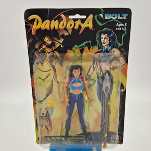 Puede incluir: Figura de acción "Pandora" de Bolt, empaquetada, para mayores de 8 años. La figura está en una funda de plástico transparente, con un respaldo de cartón colorido con ilustraciones del personaje. La figura lleva un atuendo azul y morado.