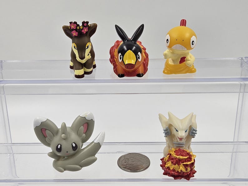 May include: Five small plastic figurines of Pokemon characters. The characters are a brown deer with a flower crown, a red and black fire-type Pokemon, a yellow and orange water-type Pokemon, a grey and white rabbit-like Pokemon, and a white and red dragon-like Pokemon.