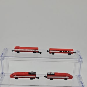 May include: Four miniature model train cars in red and white. The two front units are locomotive engines with black pantographs on top, while the two rear units are passenger carriages. Each piece features a horizontal white stripe along the side.
