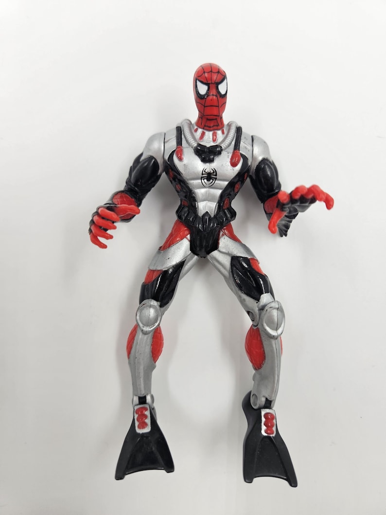 May include: A Spider-Man action figure in a diving suit. The figure is red, black, and silver with a spider emblem on the chest. The figure has black flippers on its feet and is posed with its arms outstretched.