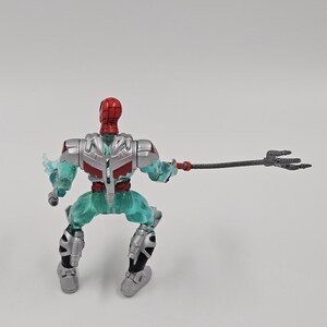 May include: A Spider-Man action figure with a red and silver helmet, red torso, and teal legs. The figure is holding a black trident. The figure is in a crouching position.