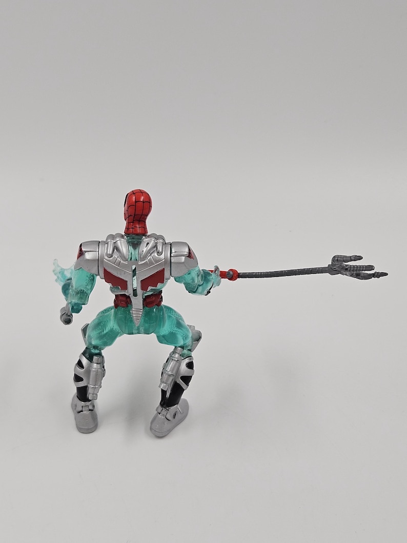 May include: A Spider-Man action figure with a red and silver helmet, red torso, and teal legs. The figure is holding a black trident. The figure is in a crouching position.