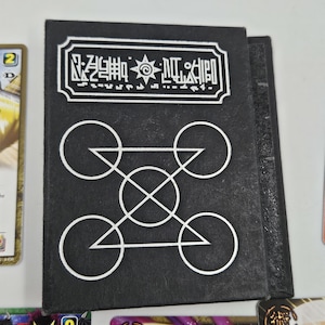 May include: Black card holder with white geometric designs and text. The top of the holder has a rectangular border with symbols and text. Below are four circles connected by lines and triangles.
