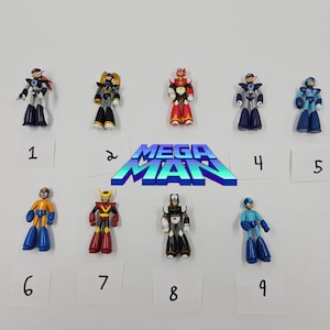 Puede incluir: Una colección de nueve figuras de acción de Mega Man en varios colores, incluyendo azul, rojo, amarillo y negro. Las figuras están numeradas del 1 al 9 y están dispuestas alrededor de un logotipo de Mega Man.