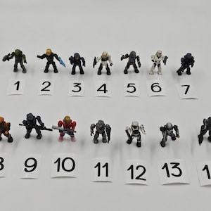 May include: Fourteen miniature action figures in various poses and colors, including green, black, orange, and white. Each figure is numbered on a small white card from 1 to 14. The figures are set against a plain white background.
