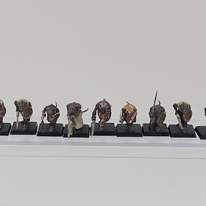 May include: A set of nine miniature rat-like humanoid figurines standing on square black bases. Each figure is painted with brown, grey, and tan tones, featuring small shields and various handheld weapons, arranged in a single horizontal line.