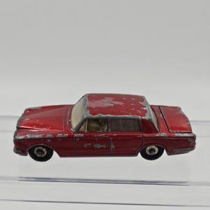 May include: A vintage red toy car with visible wear and tear. The classic sedan features four doors, black wheels, and a silver trim around the windows. The paint is chipped, giving it a well-loved appearance. A nostalgic collectible.