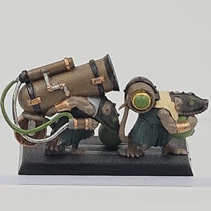 May include: Two painted miniature rat-like figures standing on a black rectangular base. The first figure carries a large bronze-colored cylindrical tank with green tubing, while the second figure carries a smaller barrel with a green circular center.