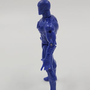 May include: A blue action figure of a humanoid robot with a detailed design. The figure has a smooth, metallic appearance with visible joints and a sculpted physique. The robot is posed in a standing position, with one hand extended.