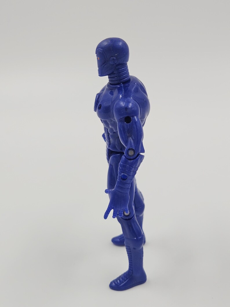 May include: A blue action figure of a humanoid robot with a detailed design. The figure has a smooth, metallic appearance with visible joints and a sculpted physique. The robot is posed in a standing position, with one hand extended.