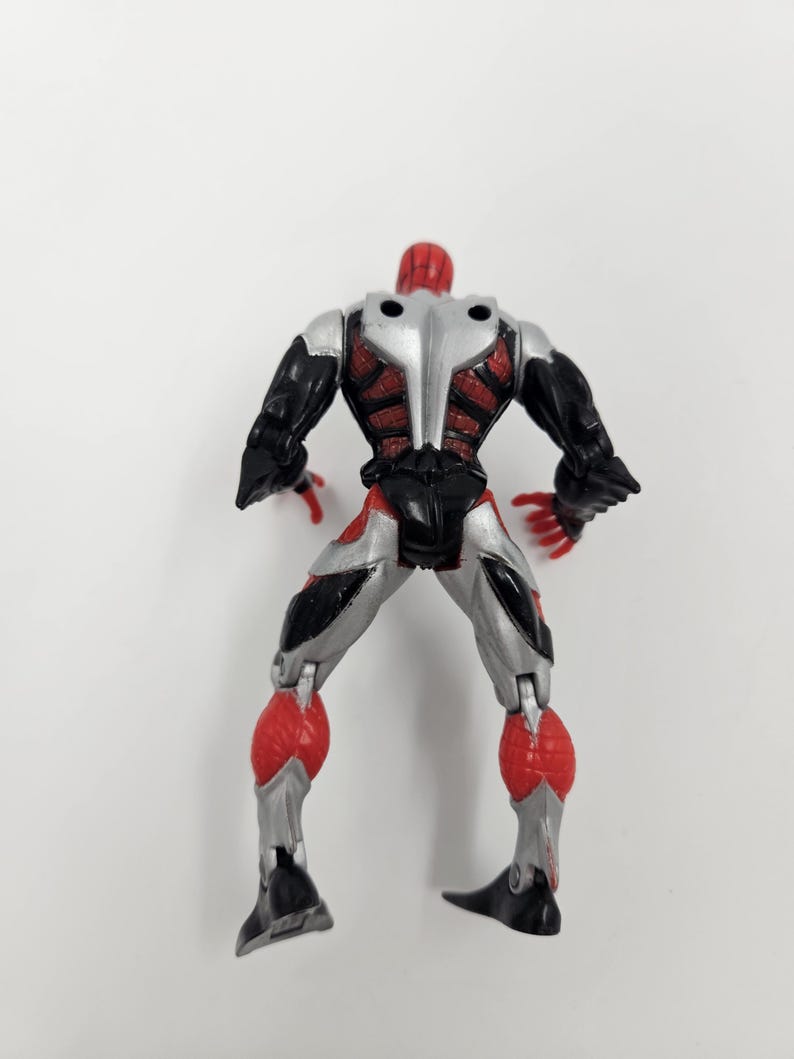 May include: A plastic action figure of a superhero, viewed from the back. The figure has a red head and hands, black arms and legs, and a silver torso. Red and silver accents are visible throughout the design.