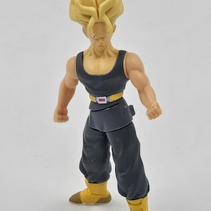 May include: A yellow-haired action figure with a black sleeveless shirt and black pants. The figure has a belt with a silver buckle and is wearing yellow boots.