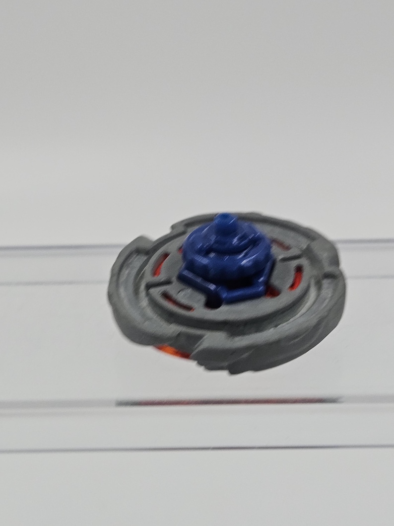 Peut inclure: Un toupie grise et rouge avec un centre bleu. Le jouet a un design circulaire avec un anneau ext&eacute;rieur textur&eacute; et un composant central sur&eacute;lev&eacute;. Le jouet est con&ccedil;u pour tourner et jouer.