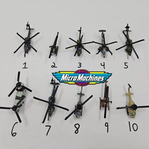以下が含まれることがあります： さまざまな色とデザインの、10機のマイクロマシンヘリコプターのコレクション。迷彩柄など。ミニチュアヘリコプターは白い面に配置されています。「Micro Machines」のロゴが見えます。