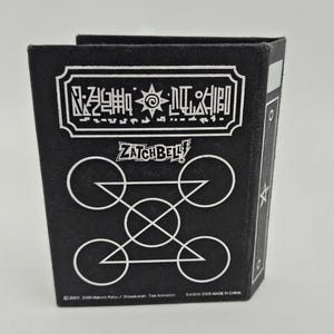 May include: Black Zatch Bell-themed box with white geometric designs and text. The box features the Zatch Bell logo and other Japanese text. The bottom of the box has copyright and manufacturing information.