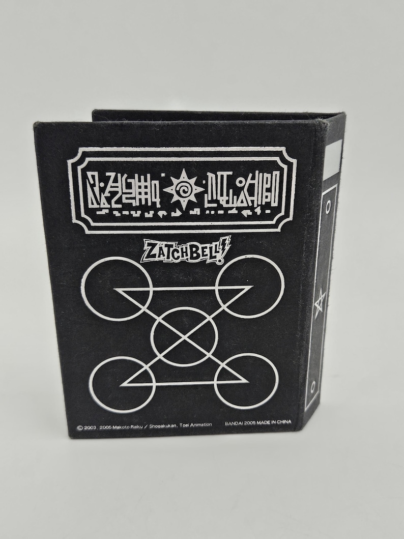 May include: Black Zatch Bell-themed box with white geometric designs and text. The box features the Zatch Bell logo and other Japanese text. The bottom of the box has copyright and manufacturing information.