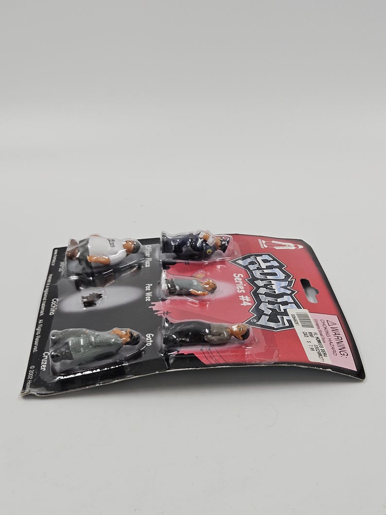 May include: A packaged set of HOMIES Series #4 figurines. The figures are in various poses and outfits. The packaging is red and black with the HOMIES logo and a warning label. The names of the figurines are Officer Place, Pee Wee, Gato, Cochina, and Cruzer.