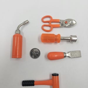 以下が含まれることがあります： オレンジとシルバーのミニチュア工具のコレクション。バーナー、ハサミ、ドライバー、やすり、ハンマー、コインが含まれています。白い表面に配置され、小さなサイズと詳細を示しています。