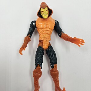 May include: Orange and black action figure of a character with a hooded cowl. The figure has an orange torso, arms, and boots, with black textured legs and arms. The face is yellow with a sinister grin.
