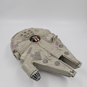 Puede incluir: Un modelo detallado de la nave espacial Millennium Falcon, con una combinación de colores gris claro con paneles y detalles intrincados. El modelo incluye una cabina, torretas de armas y otras características reconocibles de la franquicia Star Wars.