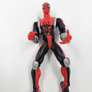 May include: A red and black Spider-Man action figure. The figure has a red head and torso with a black spider emblem. The arms and legs are black and red, with silver accents on the shoulders and knees. The figure is standing.