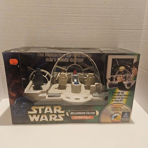 May include: A Star Wars Millennium Falcon CD-ROM playset in its original packaging. The box features the Millennium Falcon cockpit, Darth Vader, and the text "The Interactive CD-ROM Game that's hands-on FUN!" Includes a CD-ROM game and a unique Han Solo action figure.