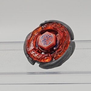 Peut inclure: Un toupie rouge et noir avec un embl&egrave;me bleu central. Le dessus a une couche ext&eacute;rieure rouge transparente et un anneau ext&eacute;rieur gris fonc&eacute;. L'embl&egrave;me pr&eacute;sente un design stylis&eacute;.