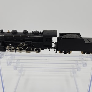 May include: A black model train with a coal car. The train is on a clear acrylic display case. The train has silver wheels and accents. The train is a steam engine style.