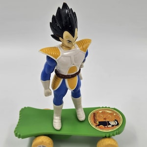 May include: A green and yellow toy skateboard with a blue and yellow action figure of a character with black hair standing on it. The skateboard has a Dragon Ball Z logo on the bottom.