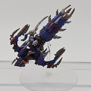 May include: A painted miniature figurine of a futuristic vehicle with a rider, featuring a blue and purple color scheme with metallic silver and bronze accents, mounted on a clear plastic flight stand with a circular base.