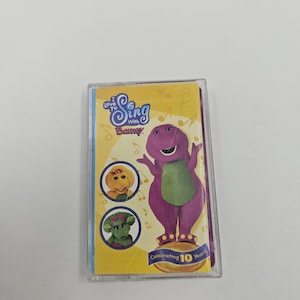 May include: A cassette tape case featuring Barney the dinosaur. The cover has the text "I Love to Sing with Barney" and "Celebrating 10 Years." The image includes Barney and two other characters. The background is yellow with musical notes.